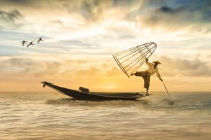 asian fisherman balancing on the end of a small boat